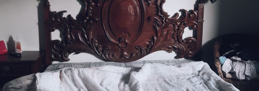 A dark wooden bed with disheveled white sheets